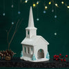 Decorative white church model with a steeple on a dark surface against a green background with lights. Decorative white church model with a steeple on a dark surface against a green background with lights.