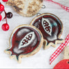 A handmade ceramic red pomegranate ornament with a dark red stoneware glaze, displayed against a festive background with Christmas decorations. A handmade ceramic red pomegranate ornament with a dark red stoneware glaze, displayed against a festive background with Christmas decorations.
